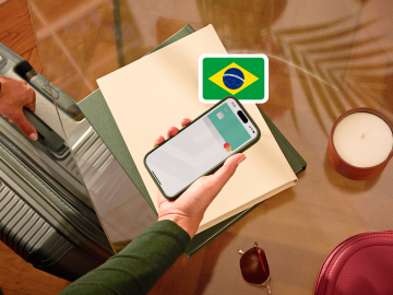 image of a person holding a phone showing an N26 card in the app screen and grabbing a suitcase with the other hand and with a brazilian flag.