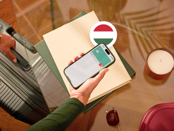 image of a person holding a phone showing an N26 card in the app screen and grabbing a suitcase with the other hand and with a Hungarian flag.