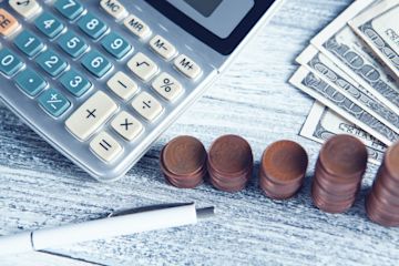 A calculator, banknotes and coins lie on a desk.