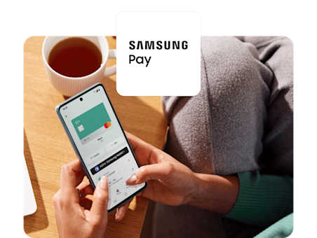 Eine Person sitzt mit einer Tasse Tee da und nutzt ihr Smartphone, um eine türkisfarbene virtuelle N26-Karte zu ihrer Samsung Wallet hinzuzufügen.