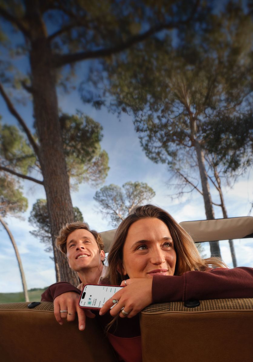 A smiling couple looks out the window of a car while holding a smartphone.
