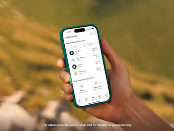 A hand holds a smartphone displaying the N26 investment screen listing popular stocks like Amazon and Apple.