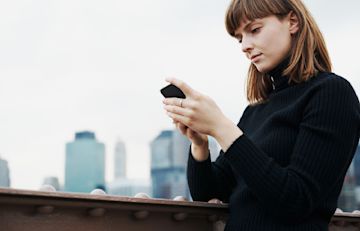 Una chica en un puente usando su teléfono móvil.