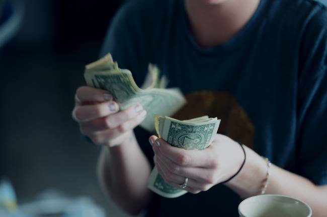 Woman is counting a stack of dollar bills with both hands.