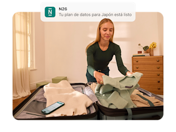 Una mujer está haciendo una maleta y mira una notificación en su teléfono que dice "N26 Tu plan de datos para Japón está listo.".