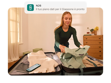 Una donna sta preparando una valigia e guarda una notifica sul suo telefono che dice "N26 Il tuo piano dati per il Giappone è pronto.