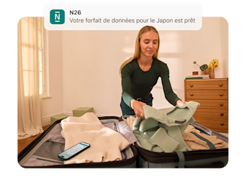 Une femme fait sa valise et regarde une notification sur son téléphone qui indique "N26 Votre forfait de données pour le Japon est prêt.".