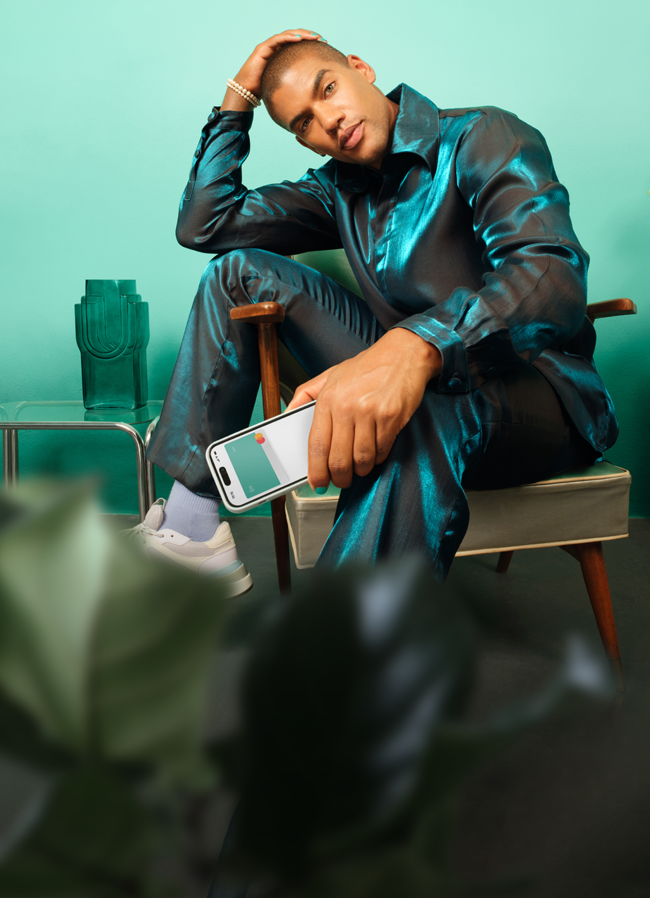 Ein Mann in einem glänzenden Kleid sitzt und hält ein Mobiltelefon, auf dem die virtuelle N26-Karte angezeigt wird.