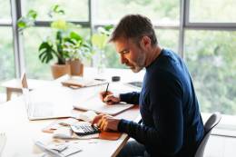 prendre des notes de l'homme travaillant avec une calculatrice et un ordinateur portable.