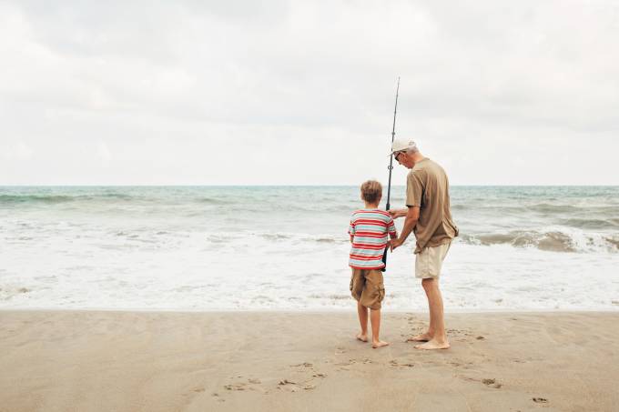 hombre mayor en la playa pescando con un niño.