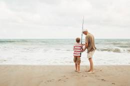 senior man in the beach fishing with a kid.