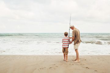 senior man in the beach fishing with a kid.
