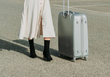 Person in a dress walking with a silver suitcase.