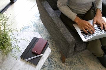 A person working on a laptop computer next to a notebook.