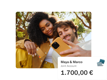 Maya and Marco sitting in a Park. Maya is holding her N26 card and Marco looking at his mobile. In the foreground there is a pop up with the amount of money in their joint account.