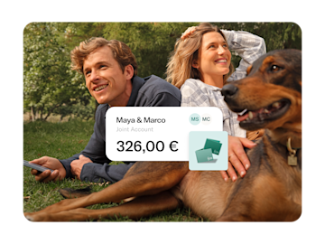 Maya and Marco are sitting in a park. Maya is petting her dog, and Marco is holding his cell phone. In the foreground there is a pop up with the amount of money in their joint account.