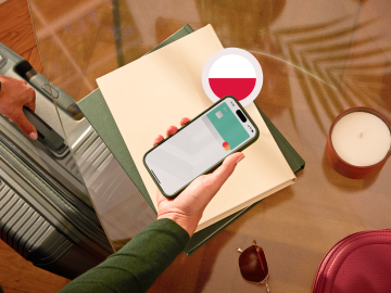 image of a person holding a phone showing an N26 card in the app screen and grabbing a suitcase with the other hand and with a Polish flag.