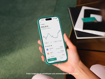 Una mano sostiene un smartphone que muestra un portafolio de criptomonedas con un gráfico de líneas y saldos.