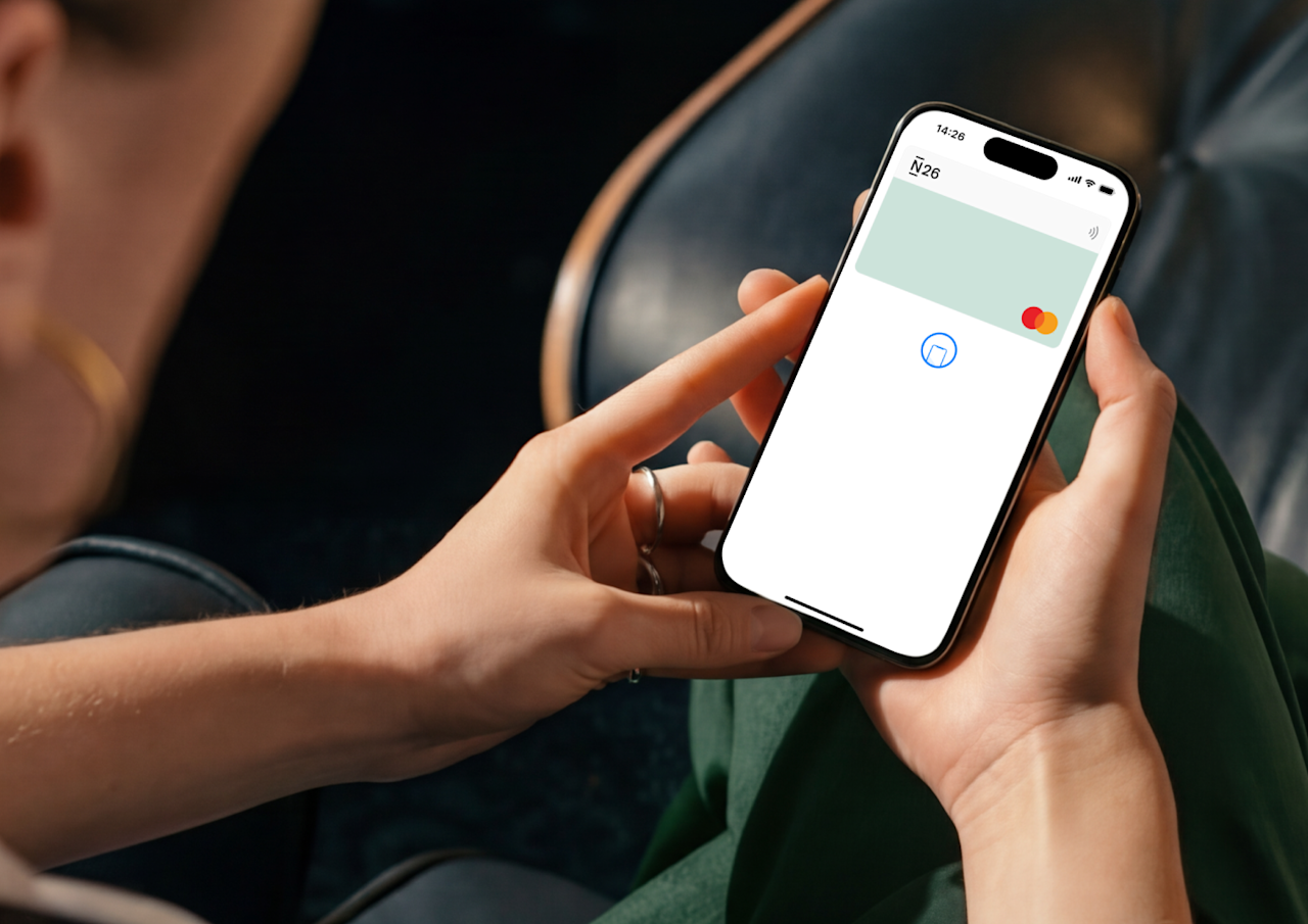 A person holds a smartphone displaying a virtual N26 Mastercard on the screen, ready for a contactless mobile payment.