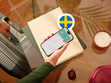 image of a person holding a phone showing an N26 card in the app screen and grabbing a suitcase with the other hand and with a Swedish flag.