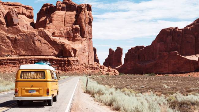 Gelber Volkswagen Minibus, der durch eine kalifornische Wüste fährt.
