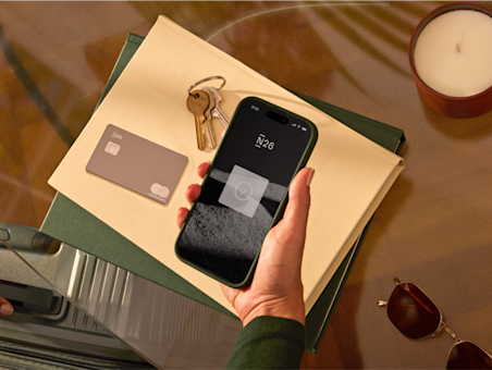 N26 app open on a phone, N26 Metal card in rhubarb, documents, candle on a glass table.