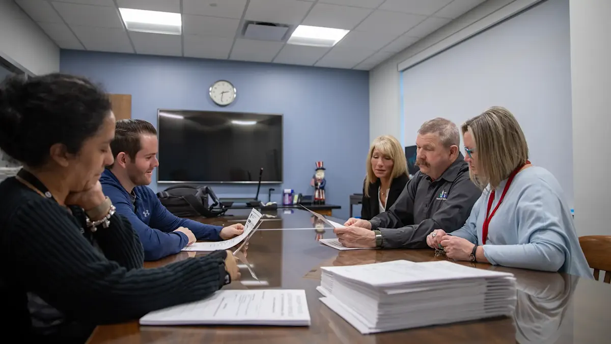 Five people review printed documents together at a conference table in a meeting room.