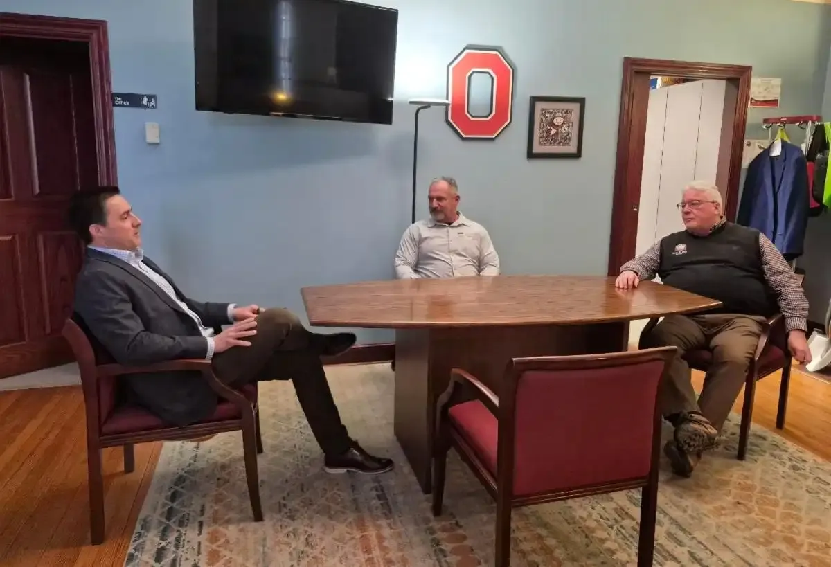 Three men seated around a small table during a discussion in an office.