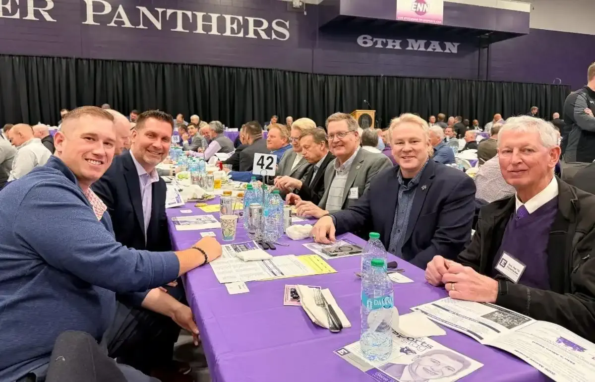 A group of men seated at a banquet table during a large indoor event.