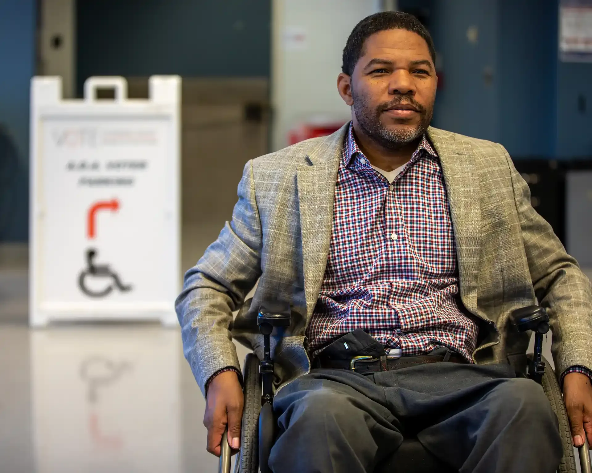 Man using a wheelchair seated indoors near an accessible voting sign.