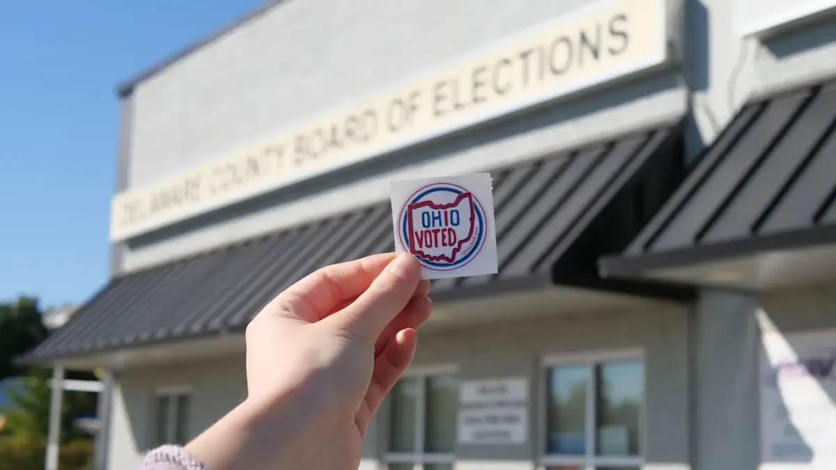 Hand holding an “Ohio Voted” sticker outside a county board of elections building.