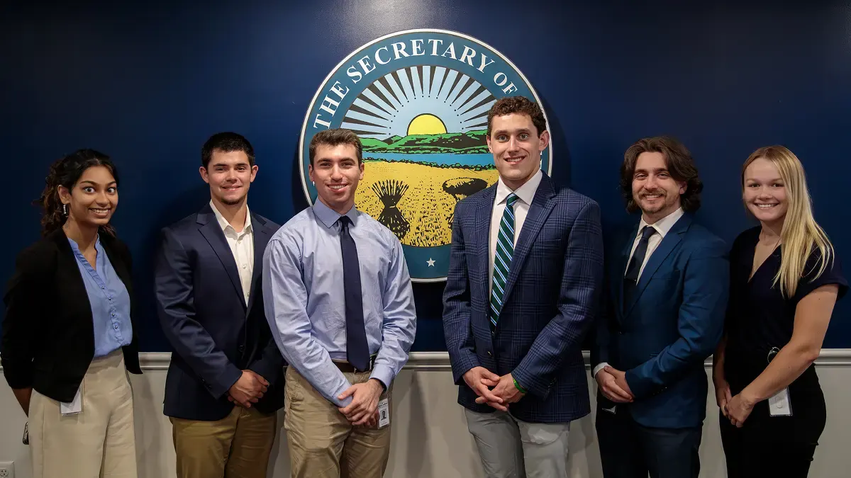 Group of interns standing in front of a Secretary of State office seal.