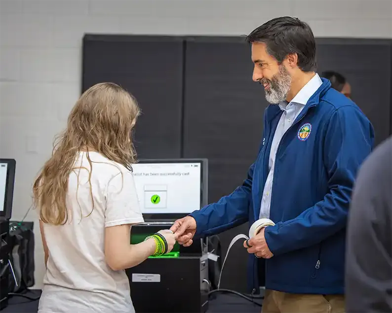 Student using a voting machine while Secretary LaRose assists nearby.