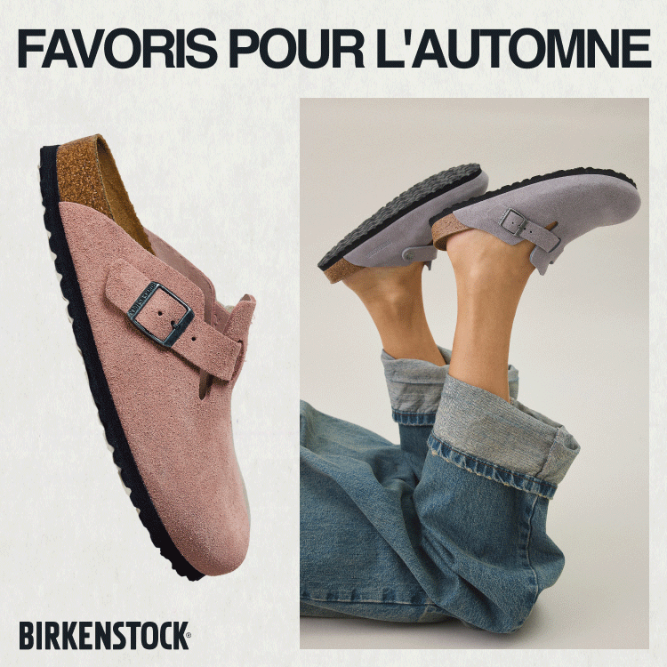 Feet wearing gray Birkenstock sandals with buckle straps and cork footbeds, paired with rolled-up jeans against beige background.