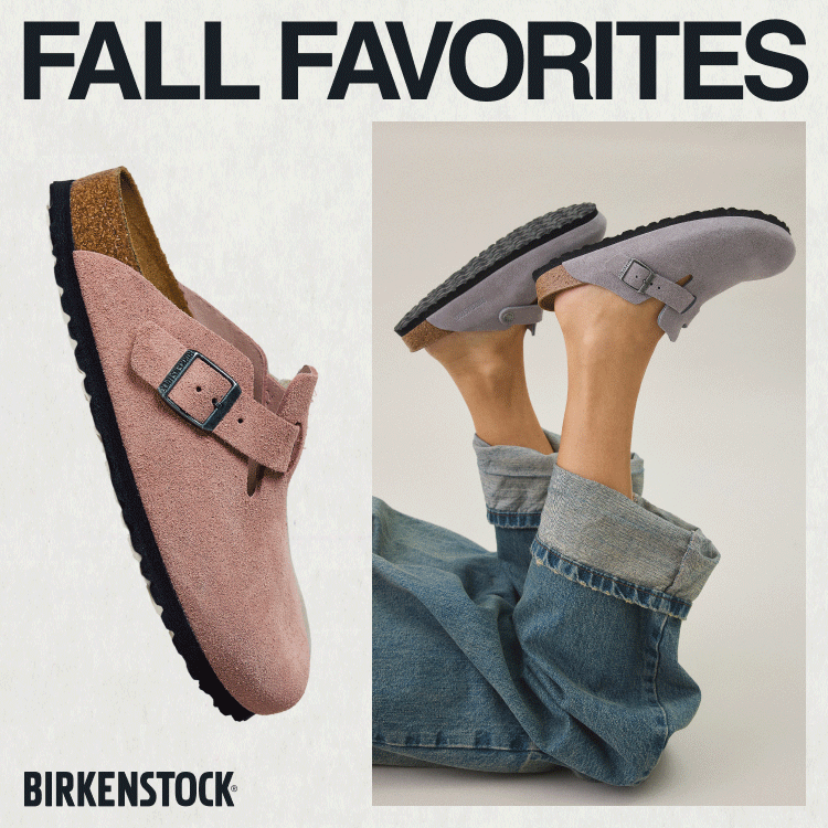 Feet wearing gray Birkenstock sandals with buckle straps and cork footbeds, paired with rolled-up jeans against beige background.