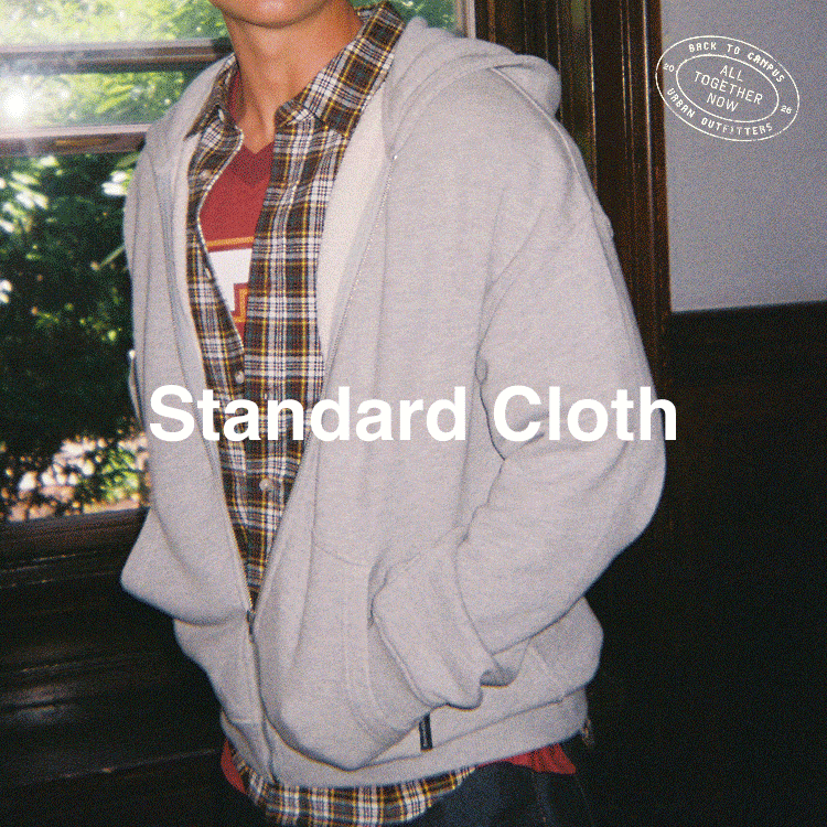 Young man in gray hoodie and plaid shirt standing indoors by window with Standard Cloth text overlay.