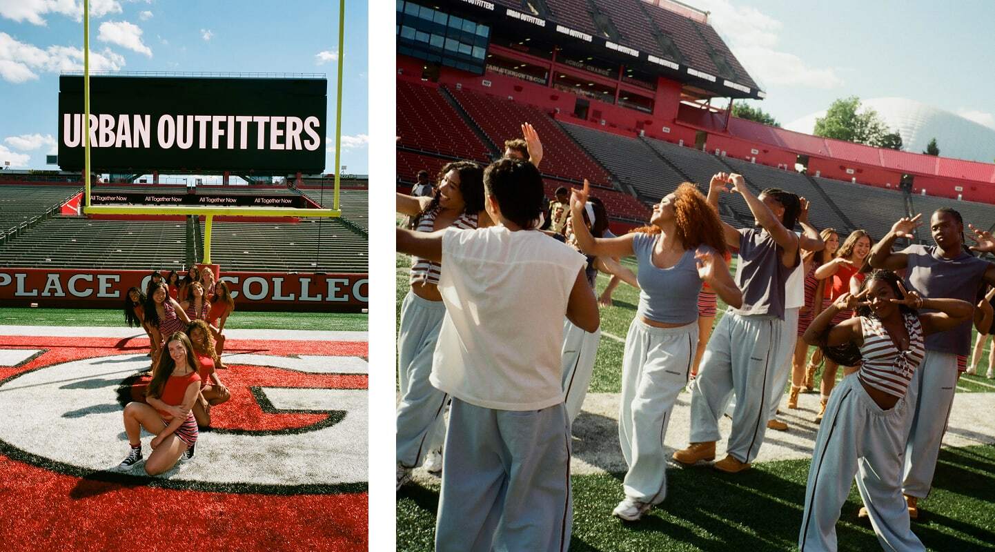 Young people posing and dancing on a football field with red stadium seating and Urban Outfitters signage visible.