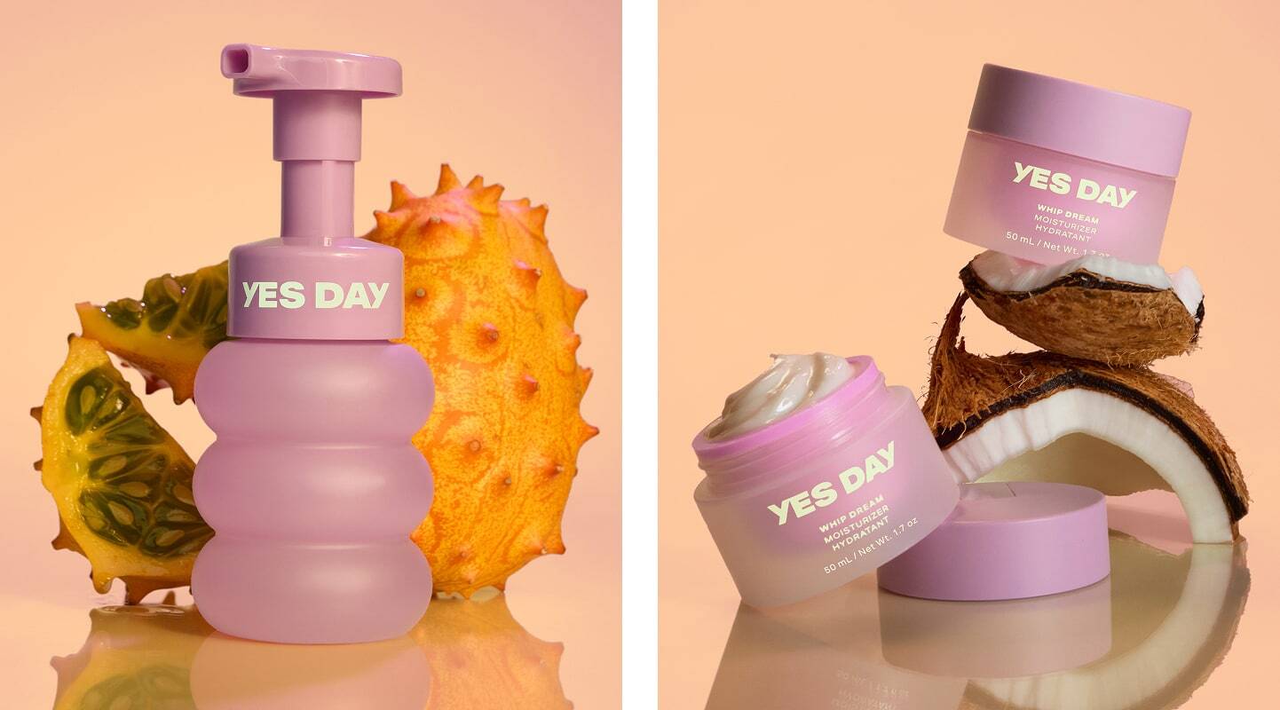 YES DAY skincare products in purple packaging displayed with tropical fruits including kiwano melon and coconut halves.