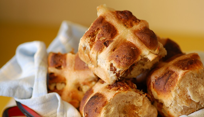 Colour photo of a stack of hot cross buns sitting on a white tea towel.