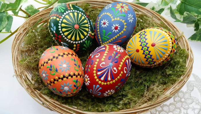 Colour photo of Easter eggs in a basket. Each egg has decorative patterns and bright colours.