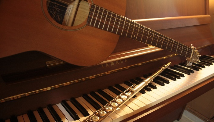 Colour photo showing a flute and acoustic guitar placed above a piano keyboard.