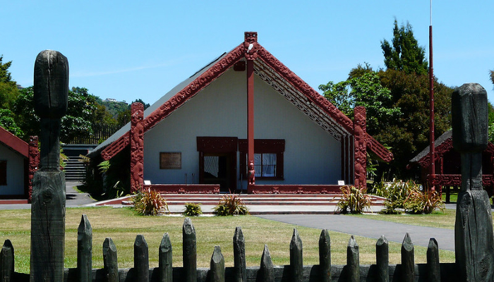 Colour photo from the Whakarewarewa village in Rotorua, Aotearoa NZ. It shows a marae ātea (courtyard) in front of a wharenui (meeting house).