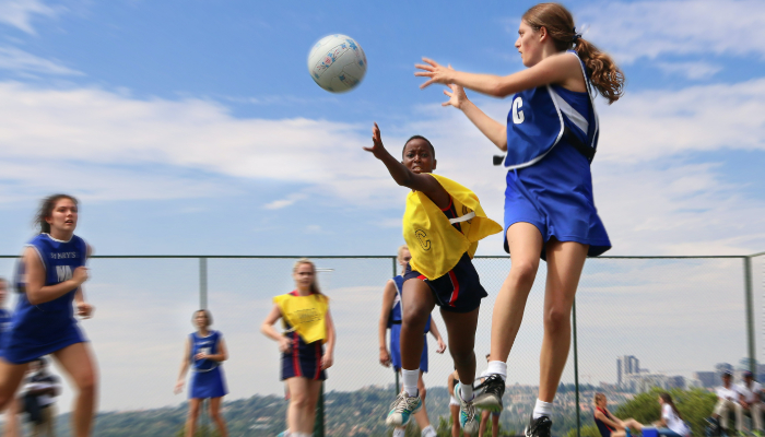 Colour photo of girls playing netball. 2 players from different teams are trying to catch a ball in the air.