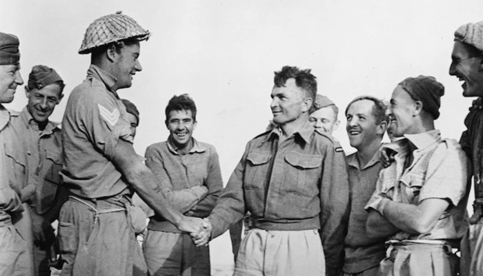 Black and white photo from 1941 showing Charles Upham being congratulated by his platoon sergeant after the presentation of the Victoria Cross. They are surrounded by members of his platoon.