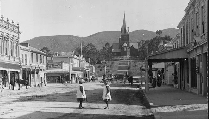 1890s photo of Trafalgar Street in Nelson. 2 girls are in the foreground. Christ Church Cathedral is on the hill at the back.