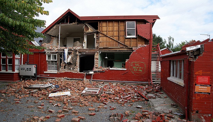 Colour photo of a two-storey house severely damaged by the 2011 Christchurch earthquake. A pile of debris lies in front of the house. 