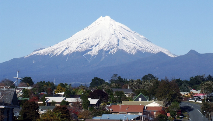 Colour photo of Mt Taranaki, Aotearoa NZ, with snow on the top. There are houses in the foreground.