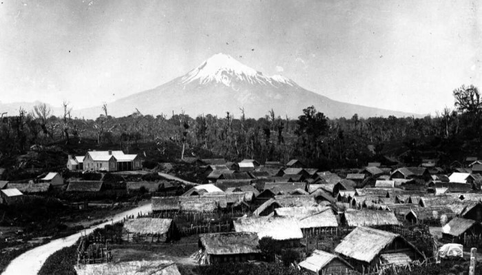 Circa 1900 black and white photo of Parihaka Pā. Mount Taranaki is in the background.