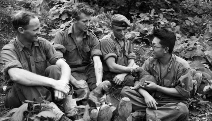Photo from 1953 of a Korean man talking to 3 Aotearoa NZ soldiers during the Korean war. The man has a puppy in his arms.