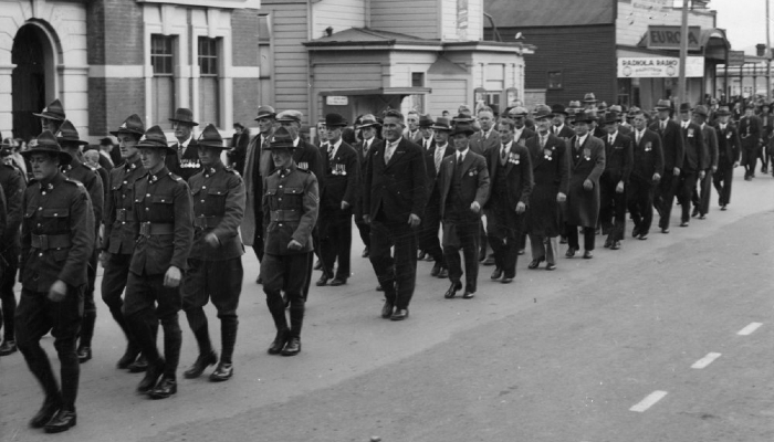 Black and white photo of an Anzac Day parade in 1937. It shows a group of people and uniformed soldiers marching on a street.